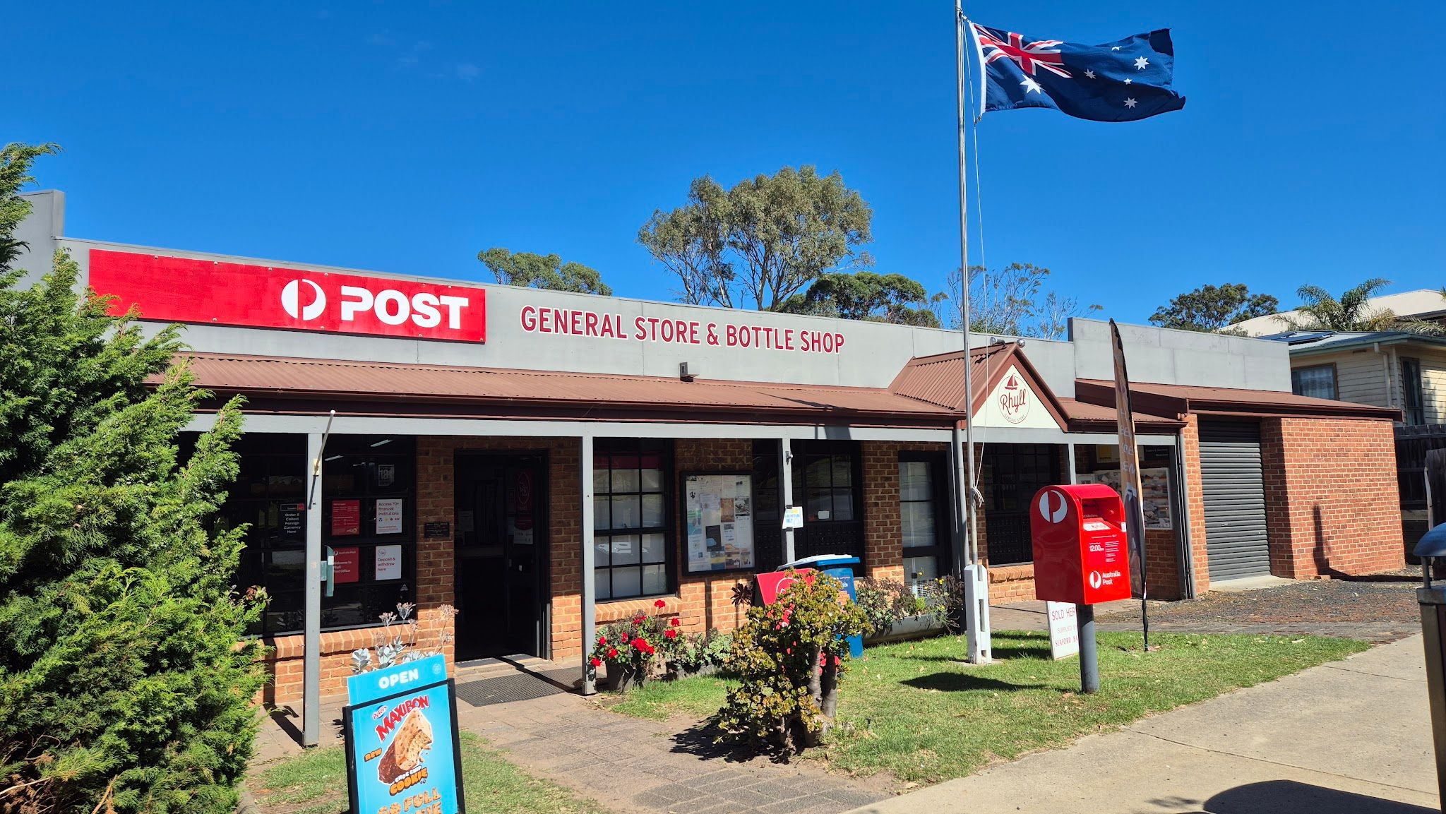 RHYLL General Store & Bottle Shop brick exterior under clear blue sky with Australian flag and post box